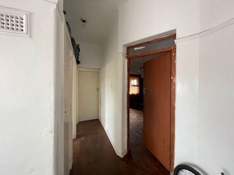 A functional hallway featuring timber flooring, built-in storage cupboards, and access to adjacent rooms, requiring cosmetic updates to improve its overall condition.