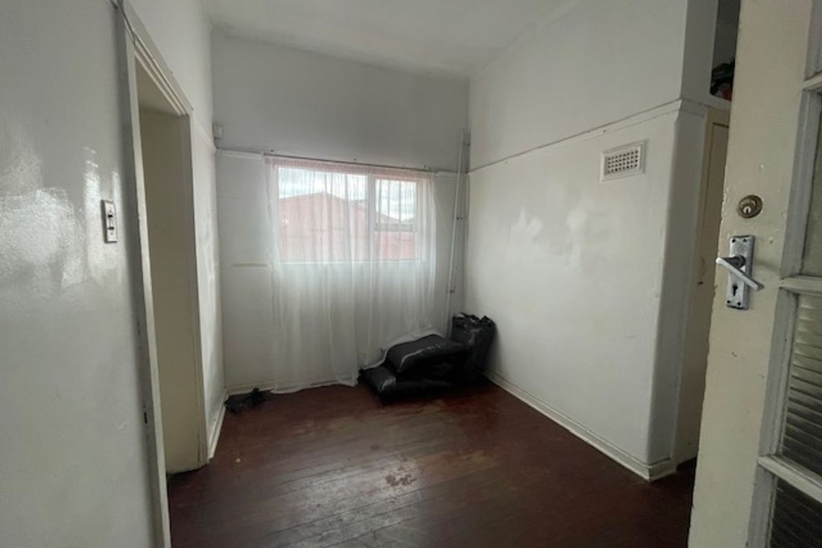 An empty bedroom featuring original timber flooring and white walls, requiring cosmetic updates and painting to restore its appeal.
