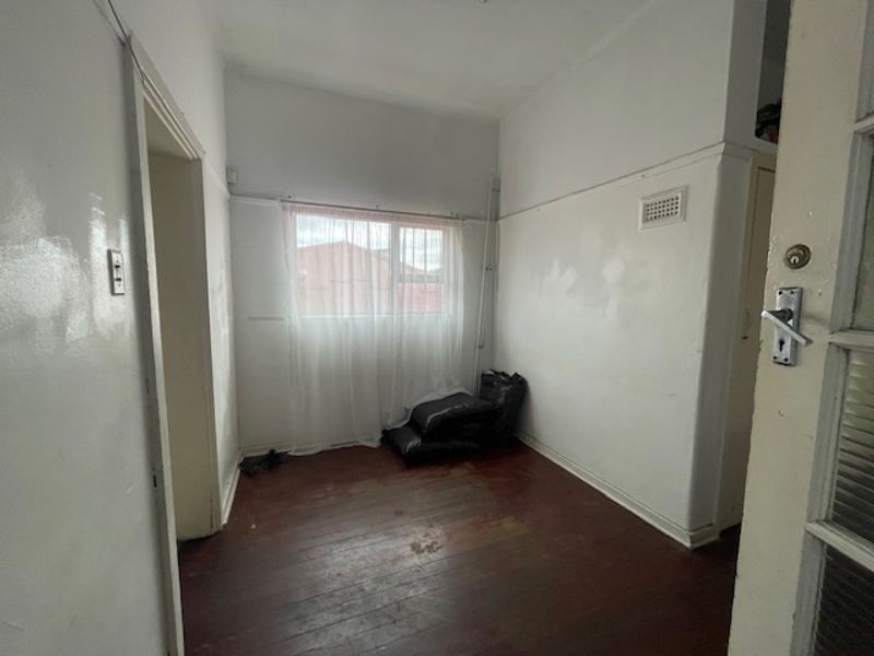 An empty bedroom featuring original timber flooring and white walls, requiring cosmetic updates and painting to restore its appeal.