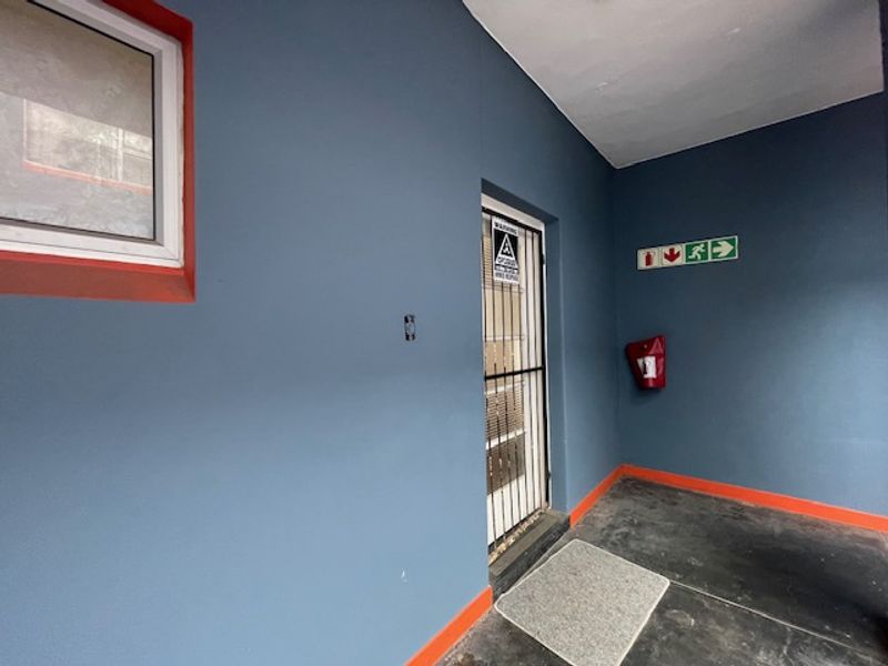 A functional building entrance area featuring a security gate, emergency signage, and a fire extinguisher mounted on the wall.