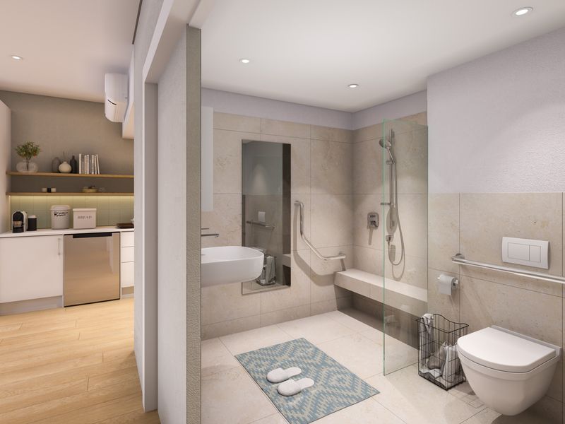 A modern, accessible bathroom featuring a walk-in shower with grab rails, wall-mounted toilet, and neutral tiling, adjacent to a compact kitchen area.