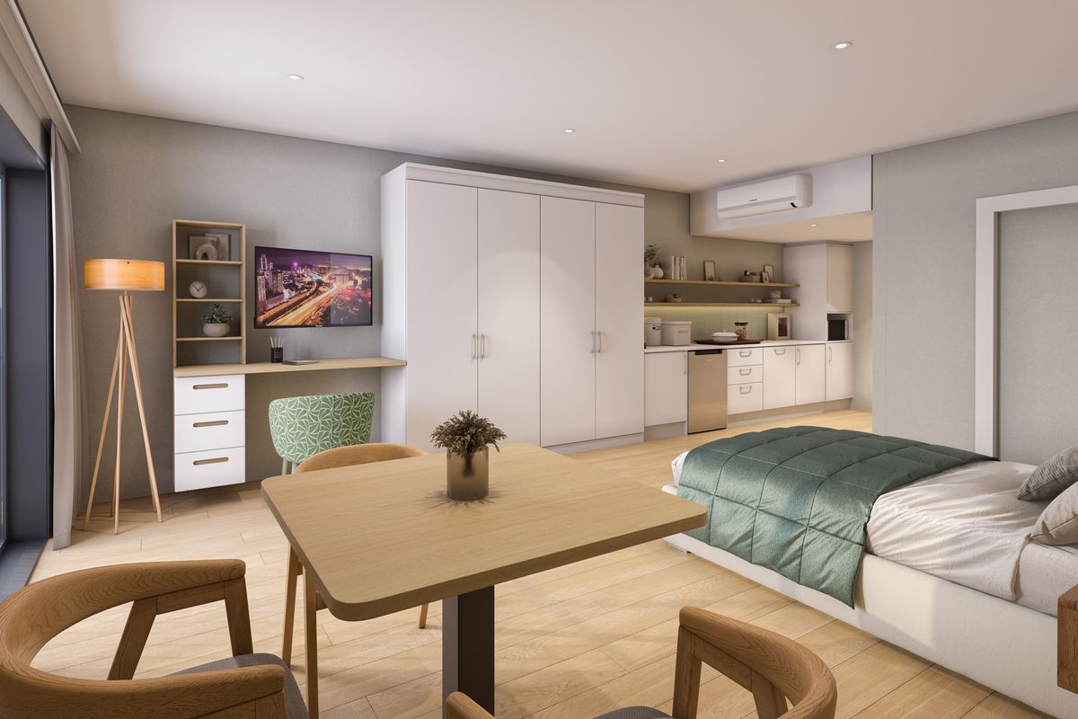 Modern open-plan studio apartment featuring a compact kitchenette, built-in storage cabinetry, light wood-look flooring, and integrated air conditioning.