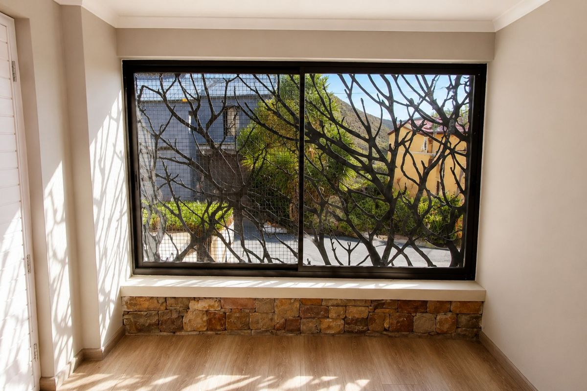 A bright, empty living space featuring a large sliding window with decorative security grille and stone-clad sill, finished with modern laminate flooring.