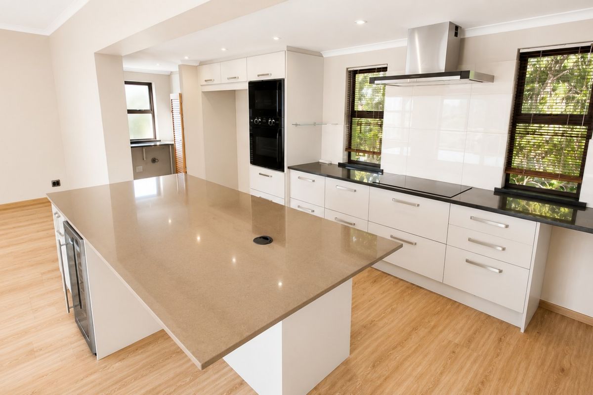 Modern, spacious kitchen featuring a large central island, stone countertops, built-in oven, extractor fan, and integrated wine cooler with light wood-look flooring.