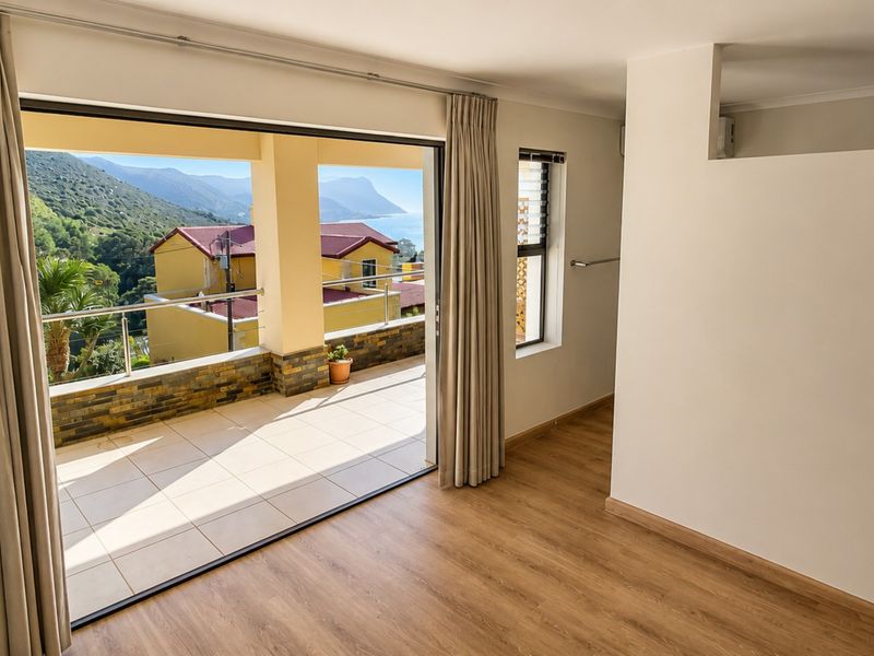 Bright, empty bedroom featuring laminate flooring and large sliding doors opening onto a balcony with scenic coastal and mountain views.