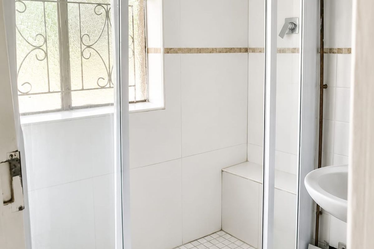 A functional bathroom featuring a walk-in shower with a built-in bench, white wall tiles, and a pedestal basin with exposed plumbing.