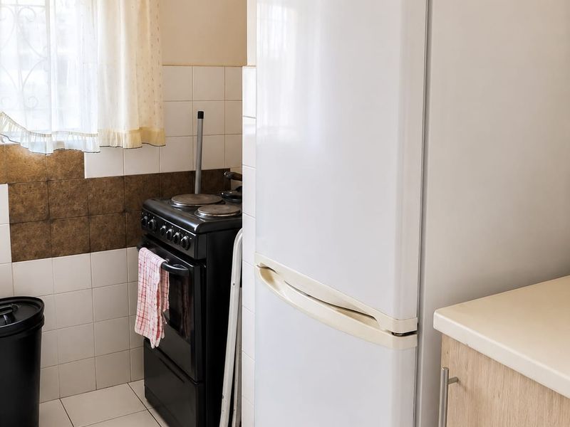 A functional kitchen featuring tiled flooring, a tiled splashback, a freestanding stove, and built-in cabinetry with laminate countertops.