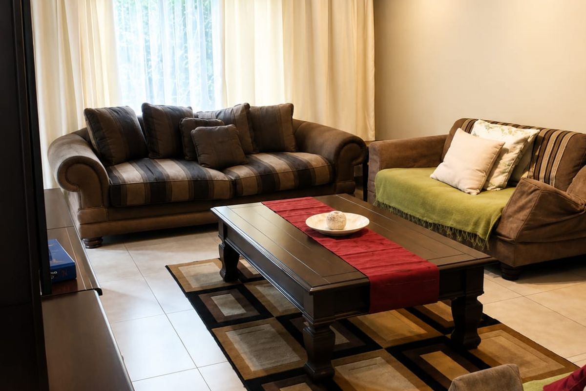 A well-lit living room featuring neutral tiled flooring and large windows with floor-to-ceiling curtains, providing a comfortable and functional space.