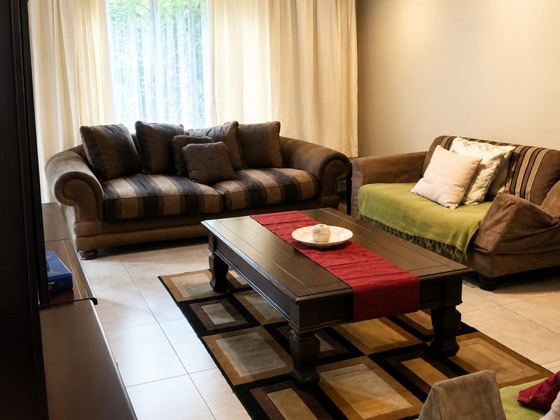 A well-lit living room featuring neutral tiled flooring and large windows with floor-to-ceiling curtains, providing a comfortable and functional space.