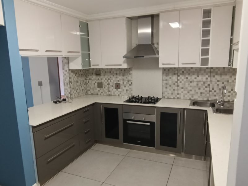 Modern kitchen featuring white and grey cabinetry, stone countertops, a gas hob, extractor fan, and a mosaic tile backsplash.