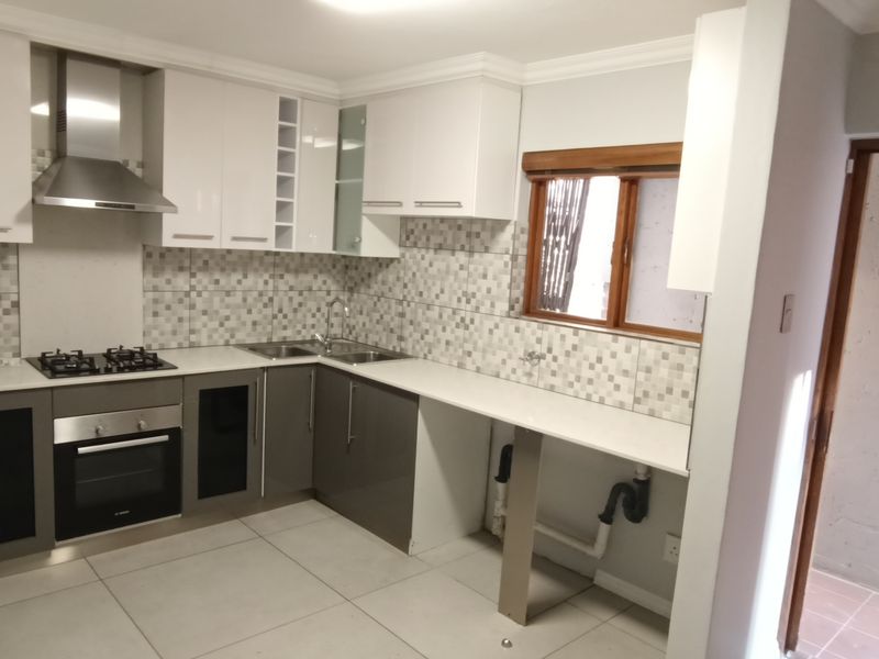 Modern kitchen featuring white and grey cabinetry, gas hob, built-in oven, stainless steel extractor, and tiled backsplash with dedicated plumbing for appliances.