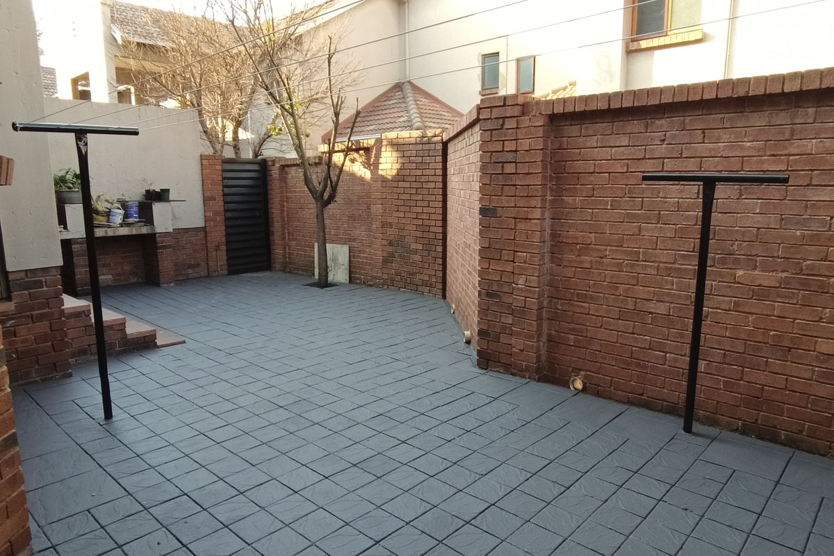 A private rear courtyard featuring paved flooring, a built-in brick braai area, and secure brick boundary walls.