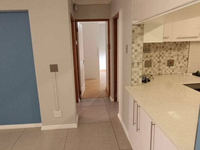 Open plan kitchen area featuring modern white cabinetry, stone countertops, and mosaic tile backsplash, leading into a hallway with tiled flooring throughout.