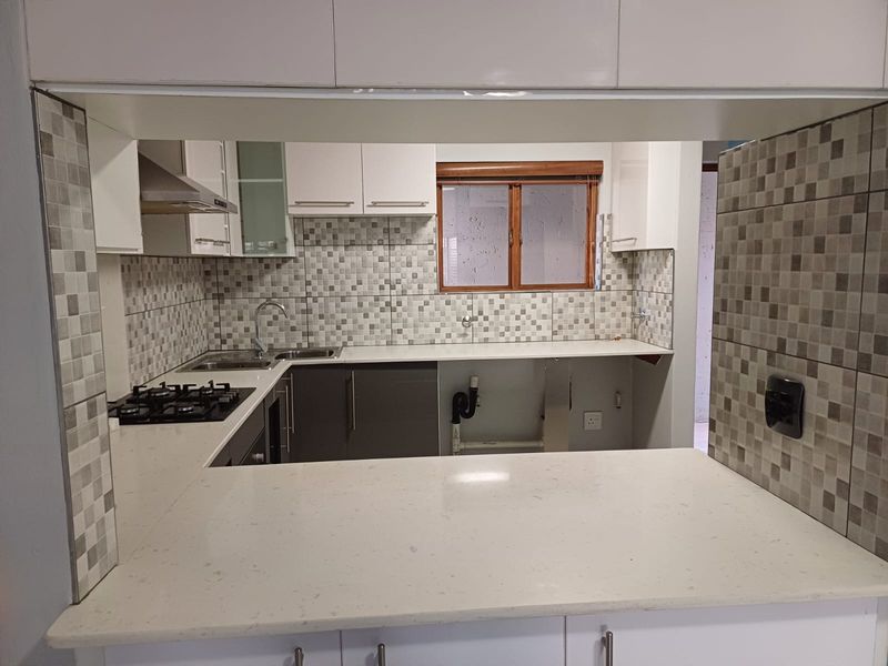 A functional kitchen featuring stone countertops, a gas hob, extractor fan, and mosaic tile backsplash, with an open-plan layout and breakfast bar.