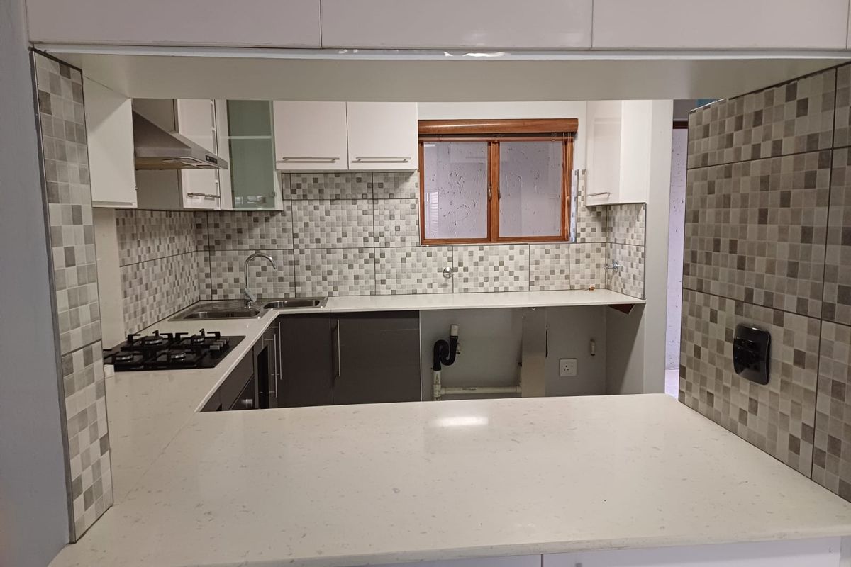 A functional kitchen featuring stone countertops, a gas hob, extractor fan, and mosaic tile backsplash, with an open-plan layout and breakfast bar.