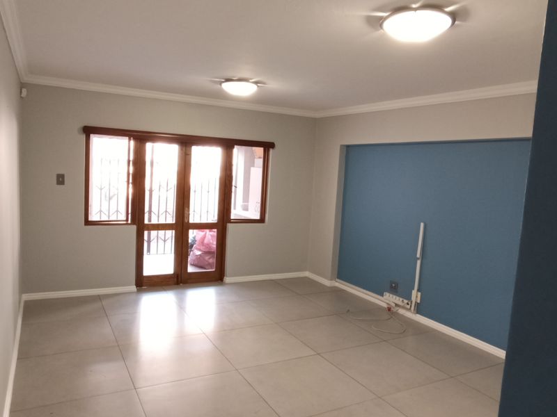 A bright, empty living room featuring large format floor tiles, neutral wall tones, and sliding glass doors with security gates leading to the exterior.