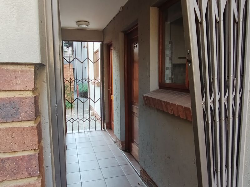 A narrow exterior entrance walkway featuring tiled flooring, a security gate, and a timber door leading into the townhouse.