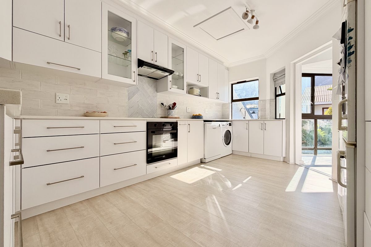 Modern kitchen featuring white cabinetry, integrated oven, extractor fan, subway tile backsplash, and dedicated laundry space with direct access to the exterior.