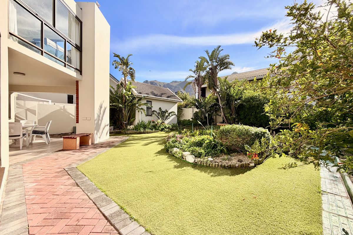 A well-maintained rear garden featuring brick paving, artificial lawn, landscaped garden beds, and a covered patio area with access to the main dwelling.