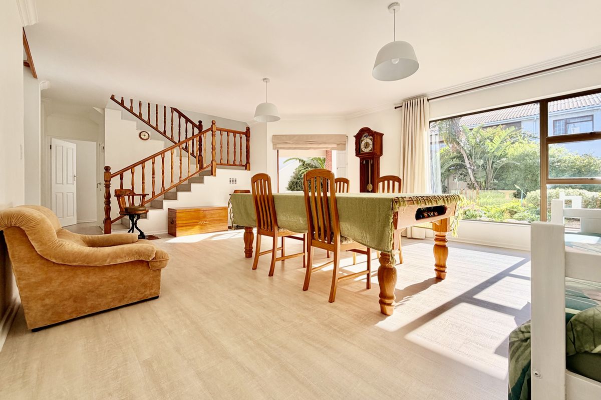 Spacious living area featuring light laminate flooring, a traditional wooden staircase with balustrade, and large sliding doors providing natural light and garden views.