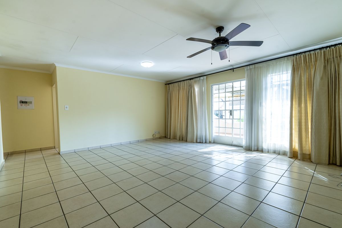 Spacious, empty living room featuring neutral tiled flooring, a ceiling fan, and large glass sliding doors providing access to the outdoor area.