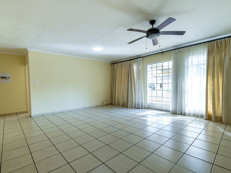 Spacious, empty living room featuring neutral tiled flooring, a ceiling fan, and large glass sliding doors providing access to the outdoor area.