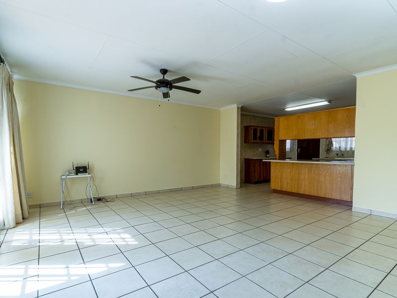Spacious open-plan living area featuring tiled flooring, a ceiling fan, and a functional kitchen with wooden cabinetry and a breakfast bar.