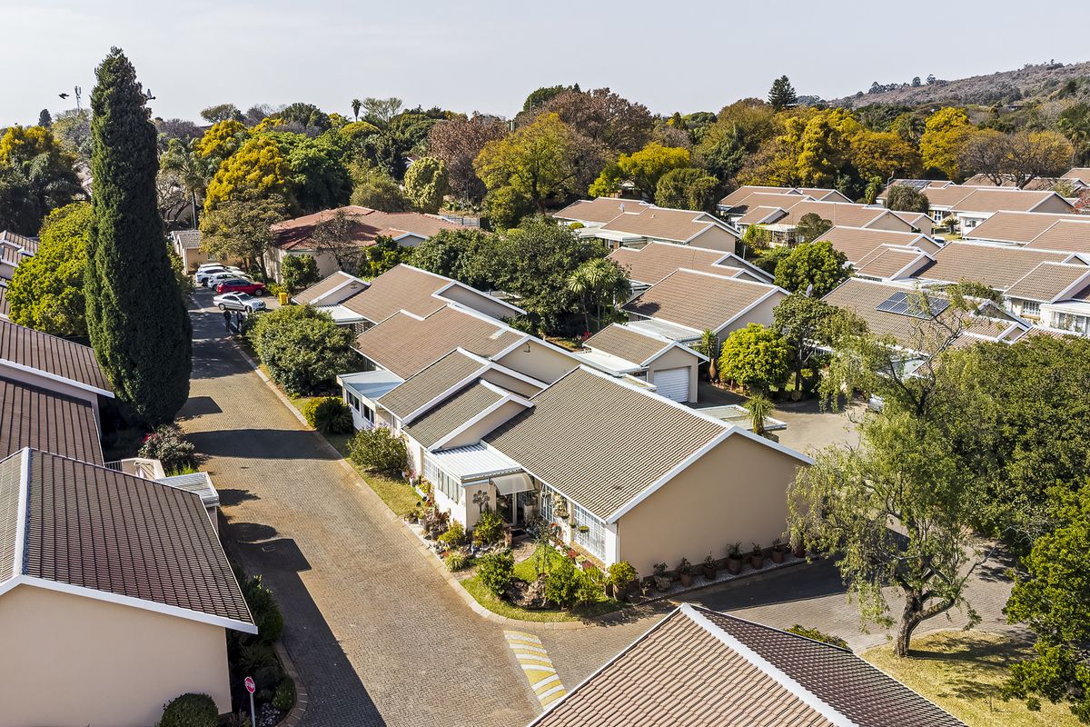 An aerial view of a well-maintained townhouse complex featuring tiled roofs, paved driveways, and established garden landscaping within a residential estate.