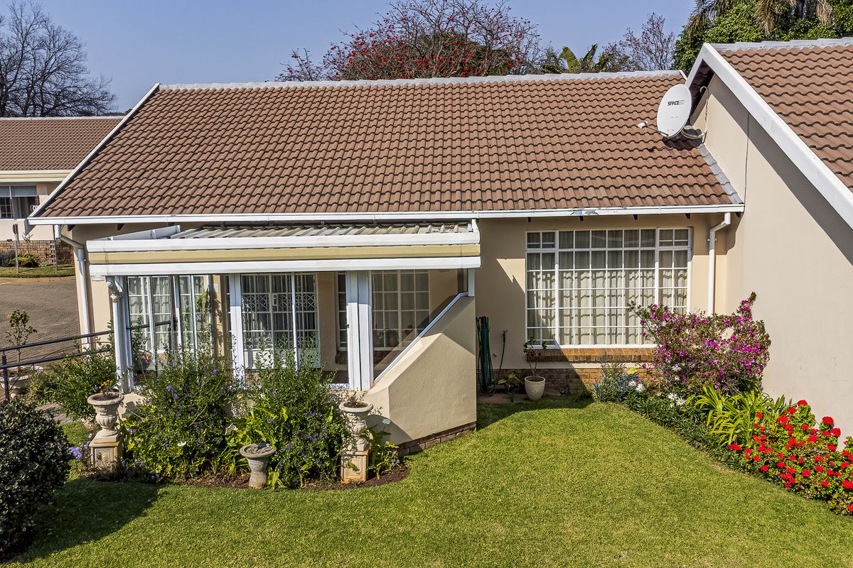 A well-maintained townhouse rear elevation featuring a covered patio, tiled roof, and a neatly landscaped garden area.