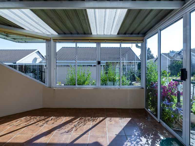 A bright, enclosed patio area featuring tiled flooring, corrugated roofing, and large aluminium sliding doors overlooking the garden.
