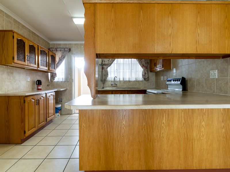 A functional kitchen featuring wooden cabinetry, laminate countertops, tiled backsplash, and tiled flooring, offering a classic layout with ample storage space.