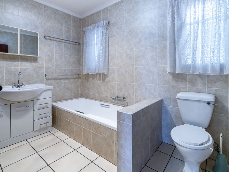 A functional bathroom featuring a built-in vanity, bathtub, and toilet with neutral wall and floor tiling.