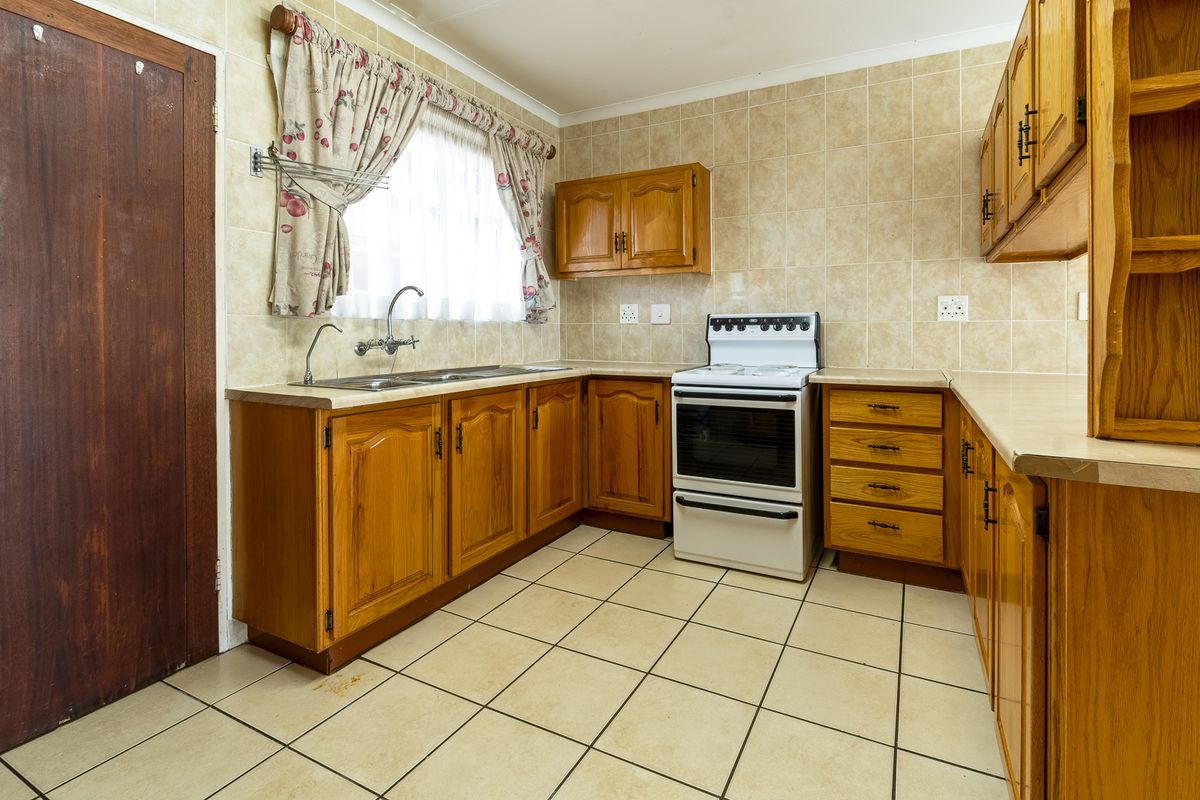 A dated kitchen featuring wooden cabinetry, laminate countertops, a double sink, and a freestanding stove with tiled splashbacks and flooring.