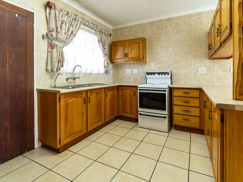 A dated kitchen featuring wooden cabinetry, laminate countertops, a double sink, and a freestanding stove with tiled splashbacks and flooring.