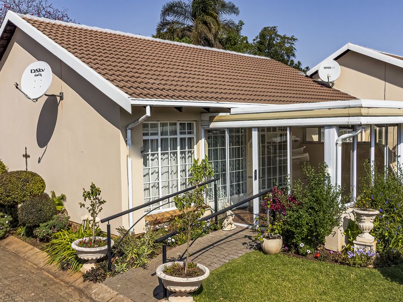 Front elevation of a townhouse featuring a tiled roof, paved walkway with handrail, and an enclosed patio area with sliding glass doors.