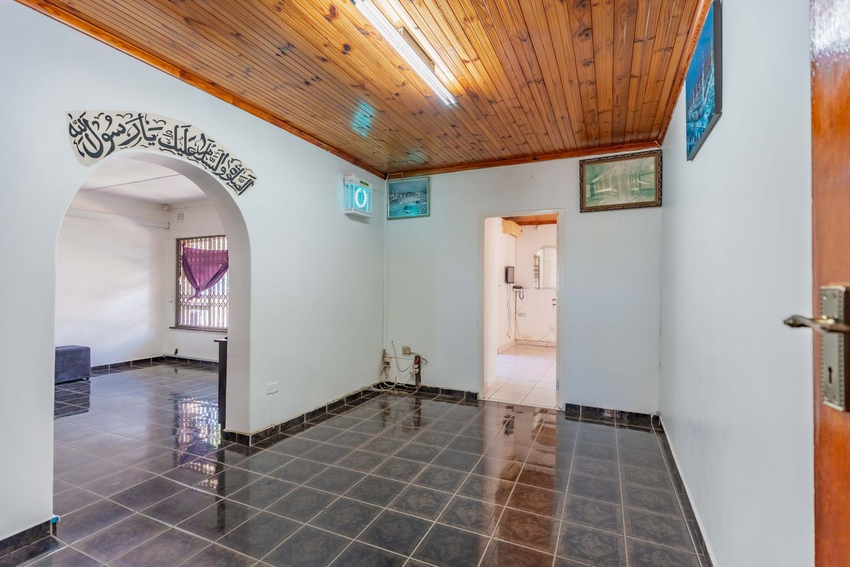 An empty living area featuring dark ceramic floor tiles and a timber tongue and groove ceiling with an arched transition to an adjacent room.