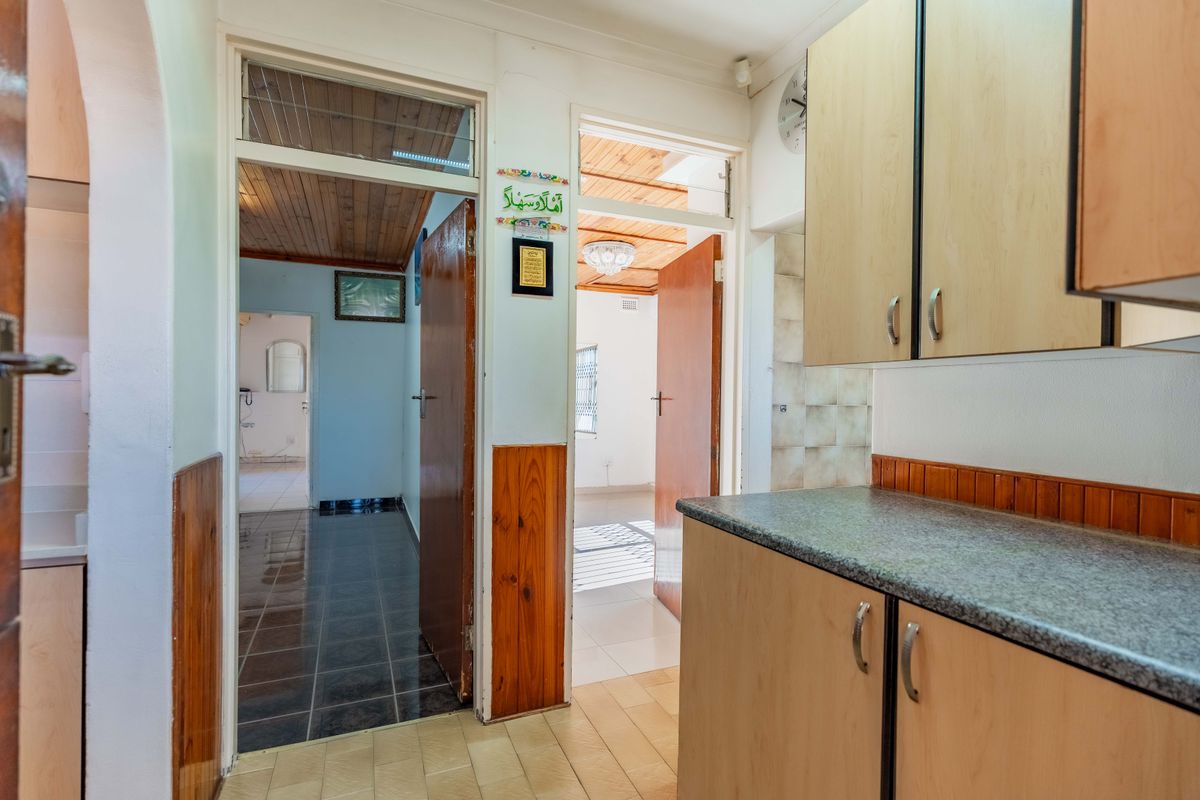 A functional kitchen area featuring timber wall paneling and cabinetry, leading into a tiled hallway and adjacent rooms with timber ceilings.