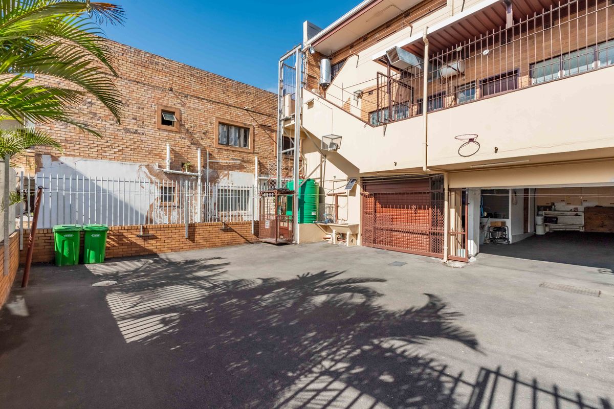 Rear exterior view of the townhouse featuring an asphalt driveway, external staircase, security fencing, and utility area with a water tank.
