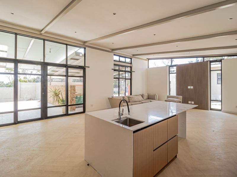 Spacious open-plan living area featuring a modern kitchen island, high ceilings with exposed beams, and large windows providing abundant natural light and outdoor access.