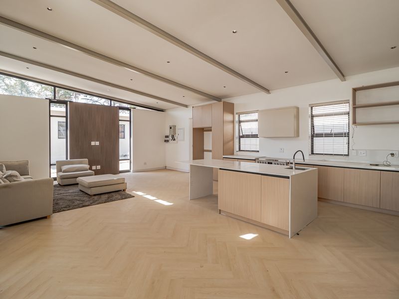 Spacious open-plan living and kitchen area featuring light wood herringbone flooring, modern cabinetry, a central island, and high ceilings with exposed beams.