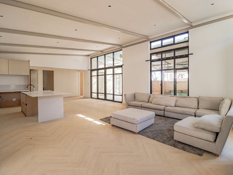 Spacious open-plan living area featuring herringbone timber flooring, exposed ceiling beams, a modern kitchen with island, and large black-framed glass doors leading outdoors.