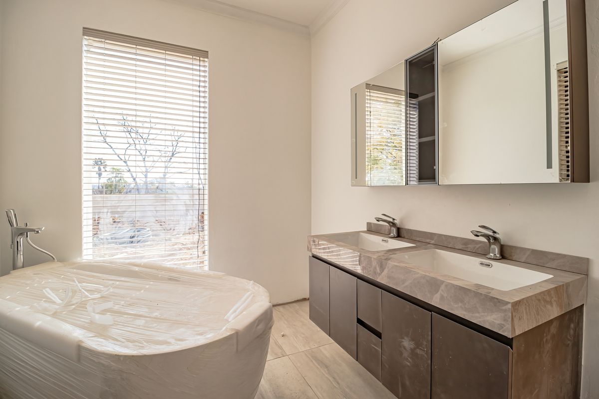 Modern bathroom featuring a double vanity with stone countertop, mirrored cabinetry, and a freestanding bathtub, currently in a clean, near-finished state.