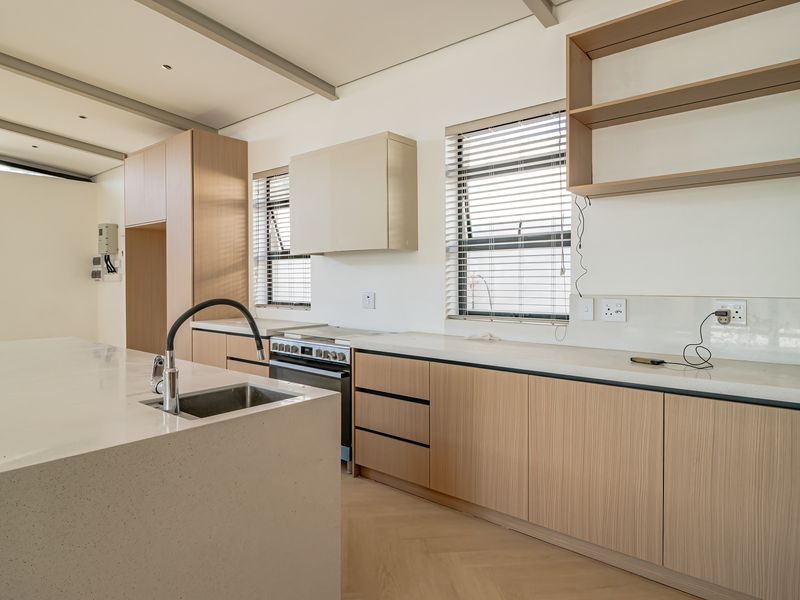 Modern kitchen featuring light timber cabinetry, stone countertops, a central island with an undermount sink, and herringbone timber flooring in a bright, open space.