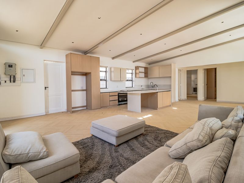Spacious open-plan living area featuring a modern kitchen with built-in cabinetry, a central island, and elegant herringbone flooring under exposed ceiling beams.