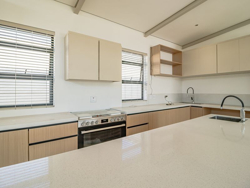 Modern kitchen featuring light wood-tone cabinetry, quartz countertops, a central island with sink, and integrated oven and hob.