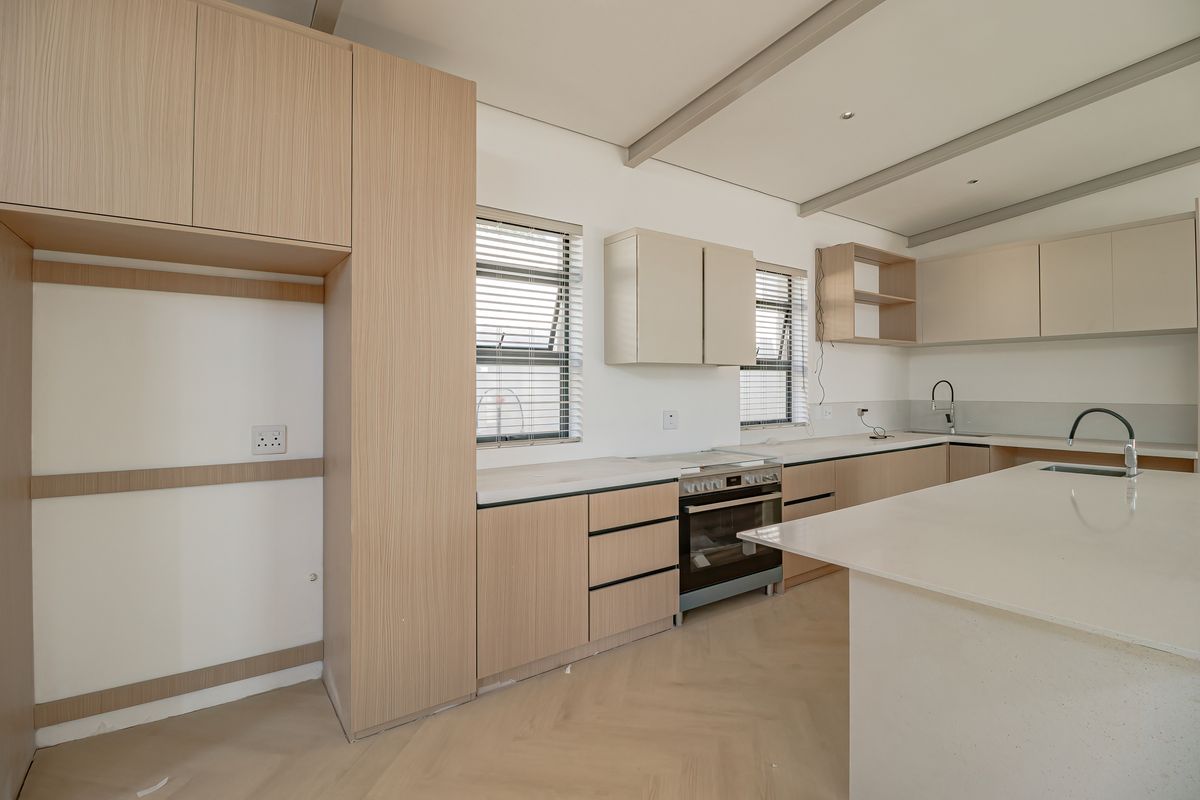 Modern kitchen featuring light wood cabinetry, stone countertops, a central island, built-in oven, and herringbone flooring in a clean, contemporary design.