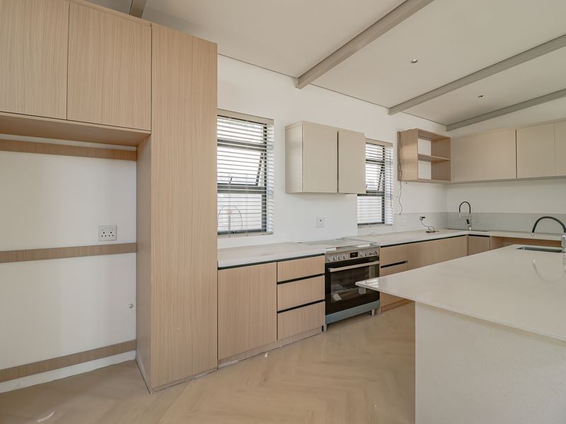 Modern kitchen featuring light wood cabinetry, stone countertops, a central island, built-in oven, and herringbone flooring in a clean, contemporary design.