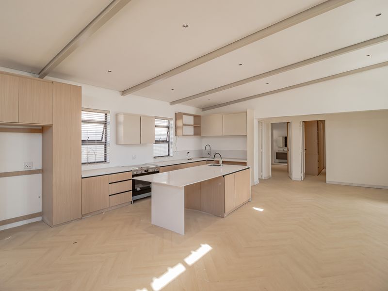 Spacious open-plan kitchen featuring light timber cabinetry, stone countertops, a central island, and modern herringbone flooring in a bright, neutral setting.