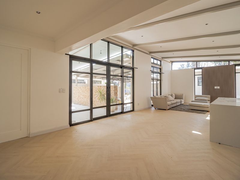 Spacious open-plan living area featuring elegant herringbone timber flooring, exposed ceiling beams, and large black steel-framed glass doors opening to the outdoors.