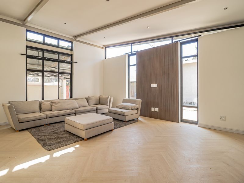 Spacious living room featuring high ceilings, herringbone timber flooring, a modern timber slat feature wall, and large black aluminium windows.